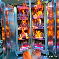 V-type gas & lava-stone doner machine · 4+4 burners · Stainless steel — Heating-bank detail during operation. The photograph shows part of the machine.